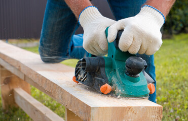 A carpenter planes a wooden board with an electric plane. Planing wooden plank with a electric...