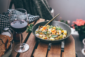 Minestrone soup on wooden table with glass of red wine outdoors. Vegetarian healthy food