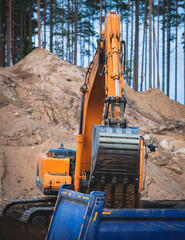 Yellow heavy excavator and bulldozer excavating sand and working during road works, unloading sand during construction of the new road