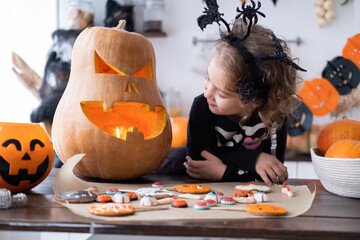 cute girl in costume of witch with pumpkin at home in kitchen, having fun, celebrating Halloween