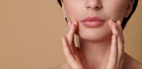 Close-up cropped beauty face portrait of beautiful European woman touching her perfect clean fresh and shiny skin near her lips. Skin care, cosmetology, SPA concept on beige background, copy space