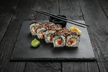 Fototapeta na wymiar Japanese cuisine. Rolls on a square plate on a black table 