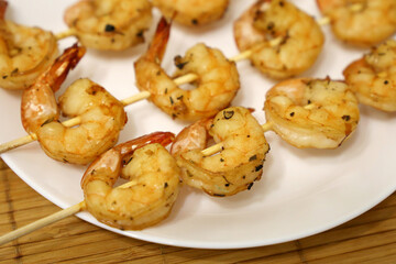 Royal shrimps grilled with spices. Wooden skewers with prawns on white plate, delicious dish