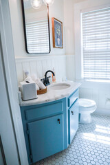 A small guest bathroom with a vintage blue vanity, retro black mirror, and clear glass light fixture in a recently renovated short term rental cottage