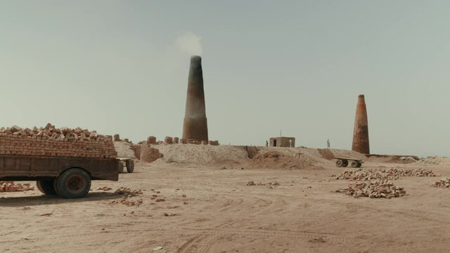 A brick factory in Pakistan that uses slave labor. On the sand there is a trailer with ready-made bricks. Against the background of the pipe from which there is smoke