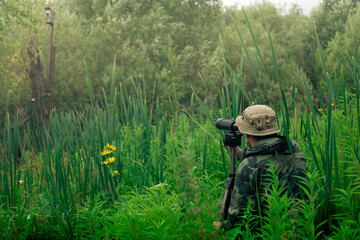 male explorer makes observations in the wild with a spotting scope standing among the tall grass