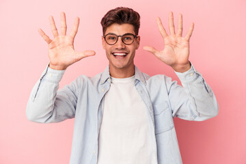 Young caucasian man isolated on pink background showing number ten with hands.