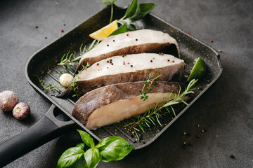 Raw halibut fish steaks with herbs and lemon prepared for cooking in a grill pan. Healthy omega 3...