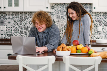 Pregnant woman with dreadlocks and her curly husband in modern kitchen cooking behind. Fresh and healthy food concept.