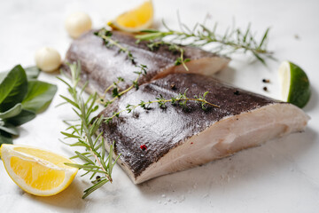 Close up of two raw halibut fish steaks with herbs and lemon on wooden board and white background. Omega 3 fats good for mental clarity. Brain food