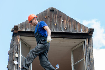 Repair of a wooden roof outdoors on a summer day against the background of blue sky and clouds. A carpenter in special clothes and with a tool installs beams and wood boards.