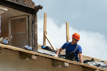 Repair of a wooden roof outdoors on a summer day against the background of blue sky and clouds. A...