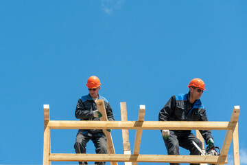 Repair of a wooden roof outdoors on a summer day against the background of blue sky and clouds. A carpenter in special clothes and with a tool installs beams and wood boards.