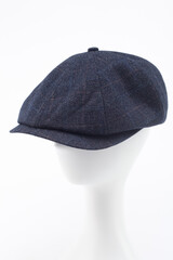 A dark blue checkered peaked cap with a visor on the head of a white mannequin. Blue checkered...