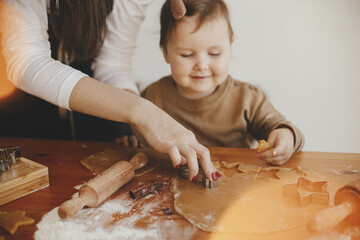 Adorable happy daughter and mother making together christmas cookies on messy table. Cute toddler girl helper with mom cutting dough for gingerbread cookies. Family preparations for xmas holidays