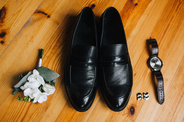 Wedding accessories and details of the groom on a wooden parquet background: black shoes, boutonniere, wristwatch,cufflinks.