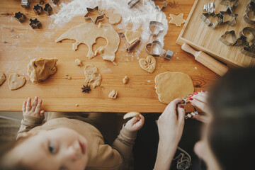 Cute daughter and mother making together christmas cookies on messy table, top view. Adorable...