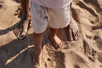 Top view of cute baby boy taking first steps while enjoying walk with dad on beach, copy space