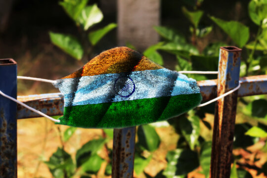 Coronavirus in India: dirty surgical mask featuring the Indian flag on an old rusty fence. Concept: Coronavirus disease (COVID-19) in India
