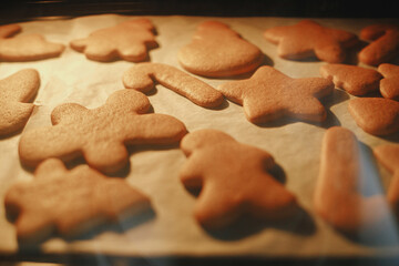 Christmas cookies baking in oven. Delicious ready gingerbread cookies on paper on tray close up in oven. Family holiday preparation, xmas culinary. Biscuits recipe
