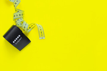 A black fitness elastic band lies on a yellow background, a measuring tape lies in rings on the side of it. top view, flat lay, copy space, isolate.