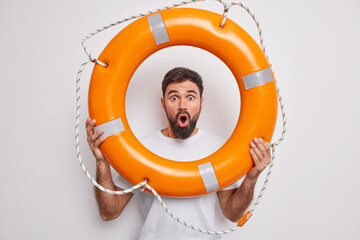 Suprised bearded man holds inflated lifebuoy stares bugged eyes wide opened mouth learns to swim...