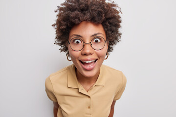 Portrait of cheerful young African American woman with curly hair looks amazed has happy surprised...