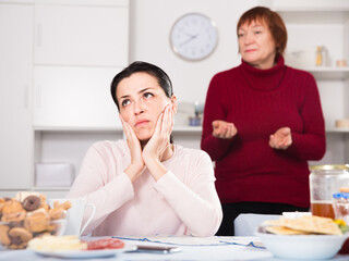 Mature female talking with young sad daughter at table with food