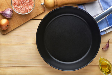 Round empty frying pan on wooden table with spices and seasoning. Griddle utensils for frying meat or vegetable. Top view with copy space for text.