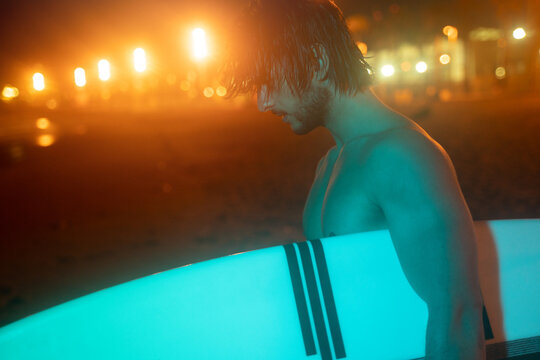 Neon green night portrait of surfer holding surf board and looking down, ready for surfing at Barcelona beach