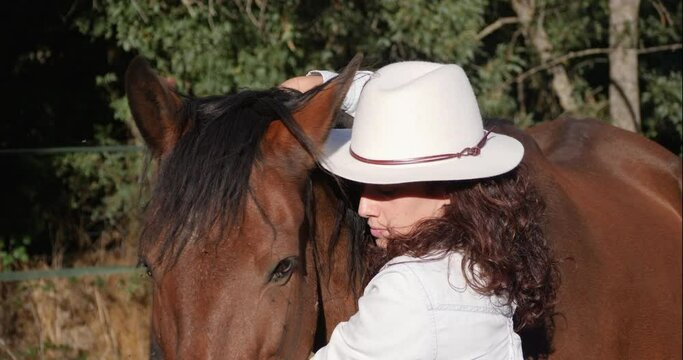 Close up of caucasian female with panama hat hugging a chestnut andalusian horse.