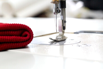 The mechanism of an industrial sewing machine. Close-up of the needle and the foot of the machine. Next to it is a red cloth.