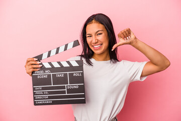 Young latin woman holding clapperboard isolated on pink background  feels proud and self confident,...