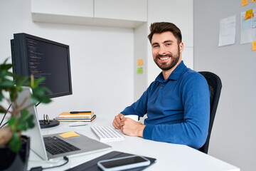 Portrait of successful computer programmer sitting at desk in office