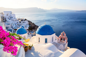 Famous Santorini iconic view. Blue domes and traditional white houses with bougainvillea flowers....
