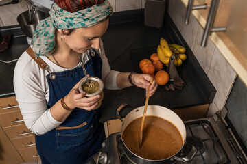 View from above of a female cook stirring the preparation of dulce de leche in the pot to prepare homemade Argentine alfajores while drinking "yerba mate tea"