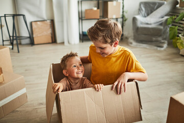 Portrait of two boys playing in big cardboard box while family moving to new house, copy space
