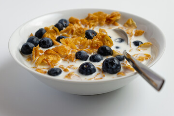 Cornflakes with blueberries and milk in a bowl on white background