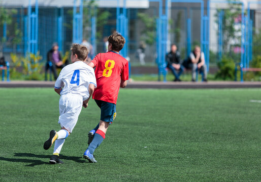 Young sport boys in red sportswear running and kicking a ball on pitch. Soccer youth team plays football in summer. Activities for kids, training