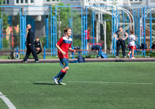 Young sport boys in red sportswear running and kicking a  ball on pitch. Soccer youth team plays football in summer. Activities for kids, training	