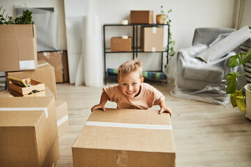 Portrait of smiling little boy moving cardboard box while family relocating to new house, copy space