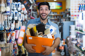 Satisfied guy handyman holding basket with tools in paint shop