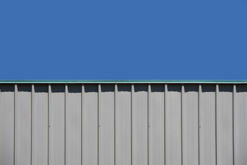 Bright blue sky seen over the roofline of a segment of an industrial warehouse