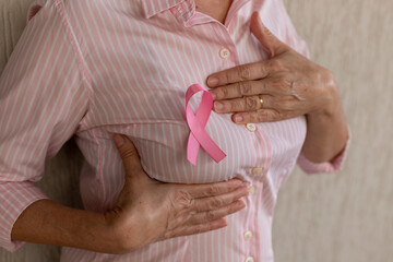 woman with pink ribbon holding hand on chest. breast self-exam. pink October.