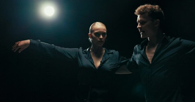 Two people spend time immersed in dancing together, a beautiful woman with blonde hair performs feminine rhythmic movements, they rotate with their partner mutually changing sides
