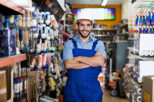 Confident workman with folded arms in paint store amongst racks with tools