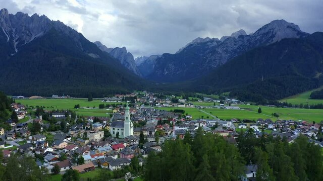 Church of San Giovanni Battista, Dolomites, Toblach, Dobbiaco, Puster Valley, Bolzano, South Tyrol, Italy, September 2021. Drone pushes forward across the town passing the copper roof church.