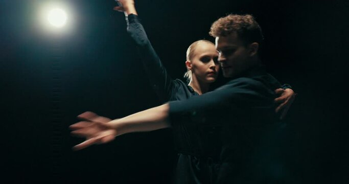 Two people spend time immersed in dancing together, a beautiful woman with blonde hair performs feminine rhythmic movements, they rotate with their partner mutually changing sides