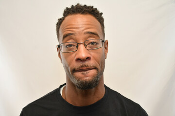 African American male wearing glasses looks into the camera while biting his lip. 
