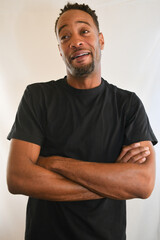 African American male in a black t-shirt looks into the camera with folded arms. 